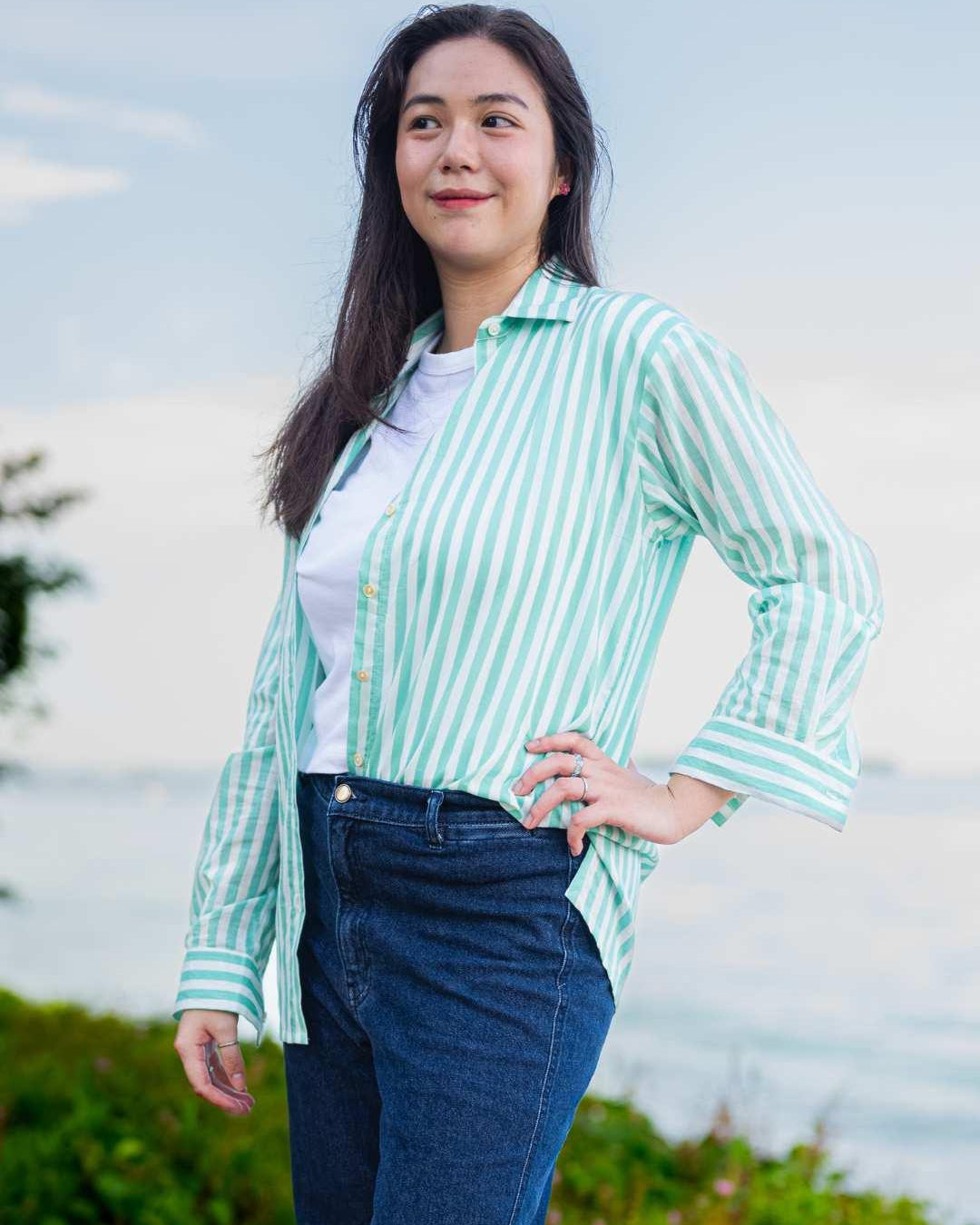 Woman wearing a green and white striped shirt with a blurred natural background