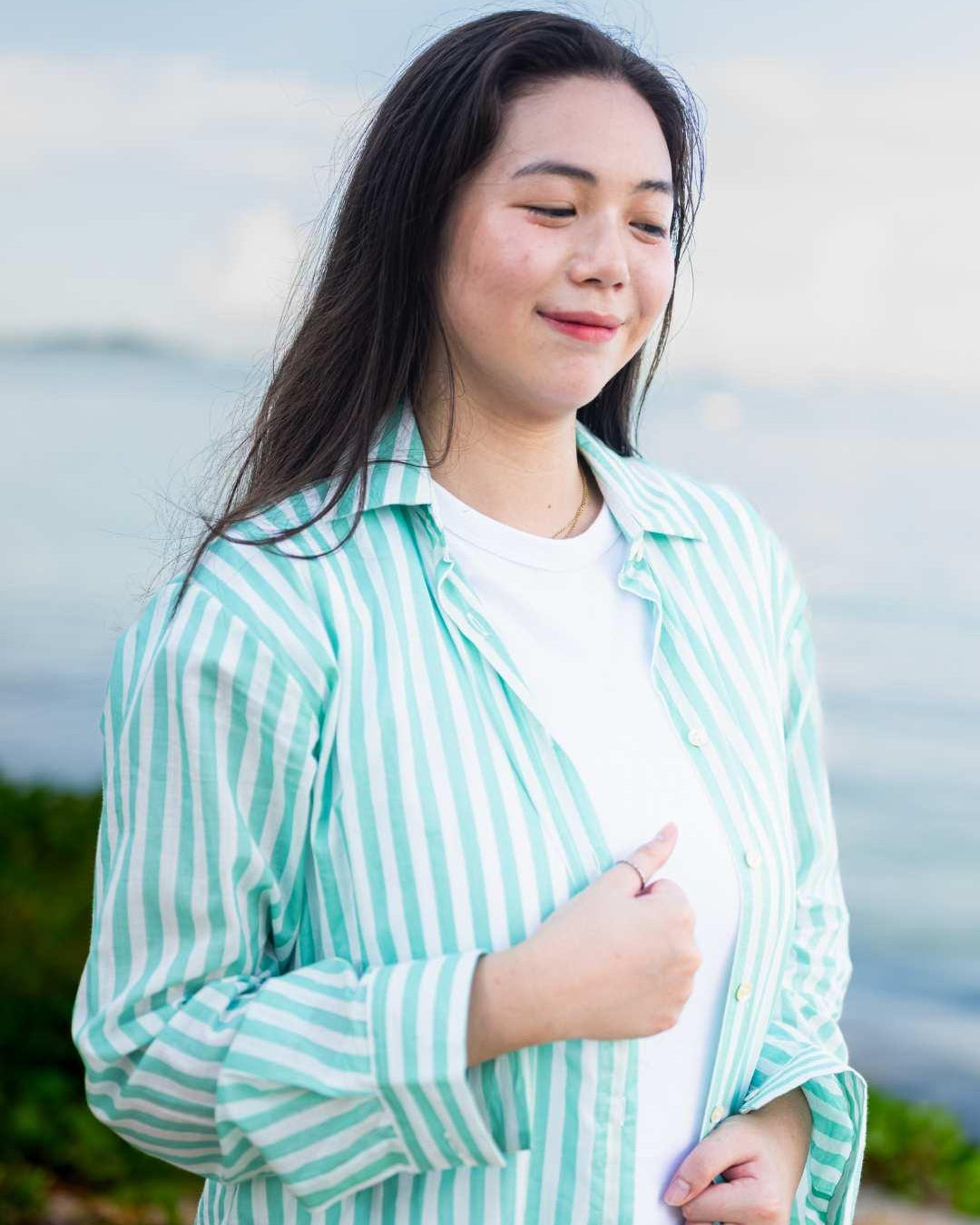 Woman wearing a green and white striped shirt by a body of water