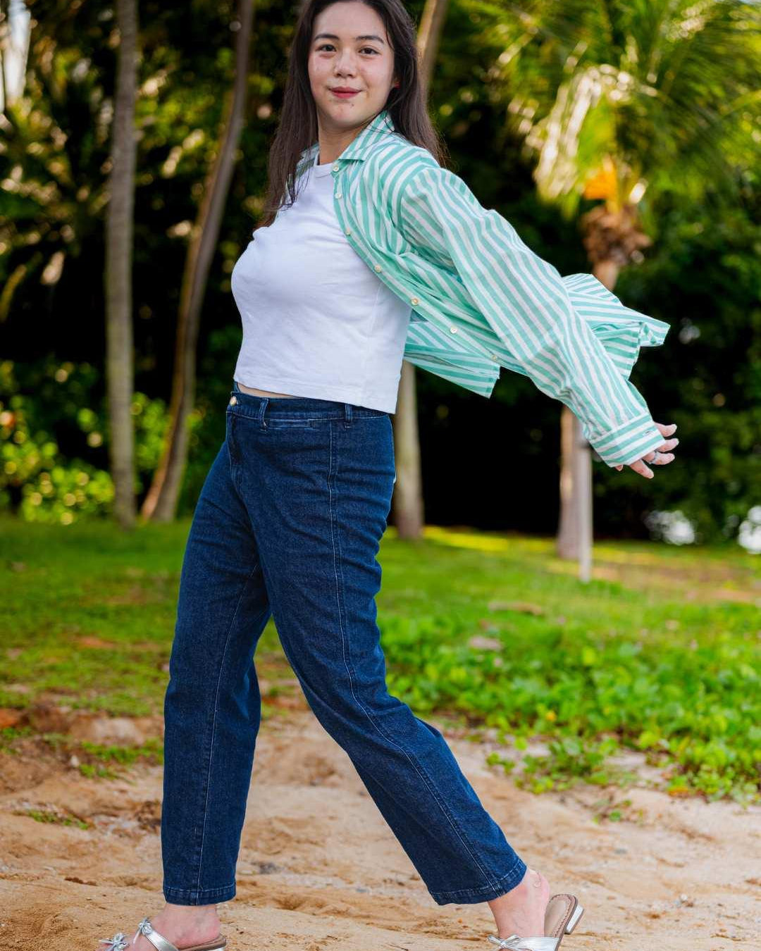 Woman wearing a white top and blue jeans with a striped green and white shirt in a park setting