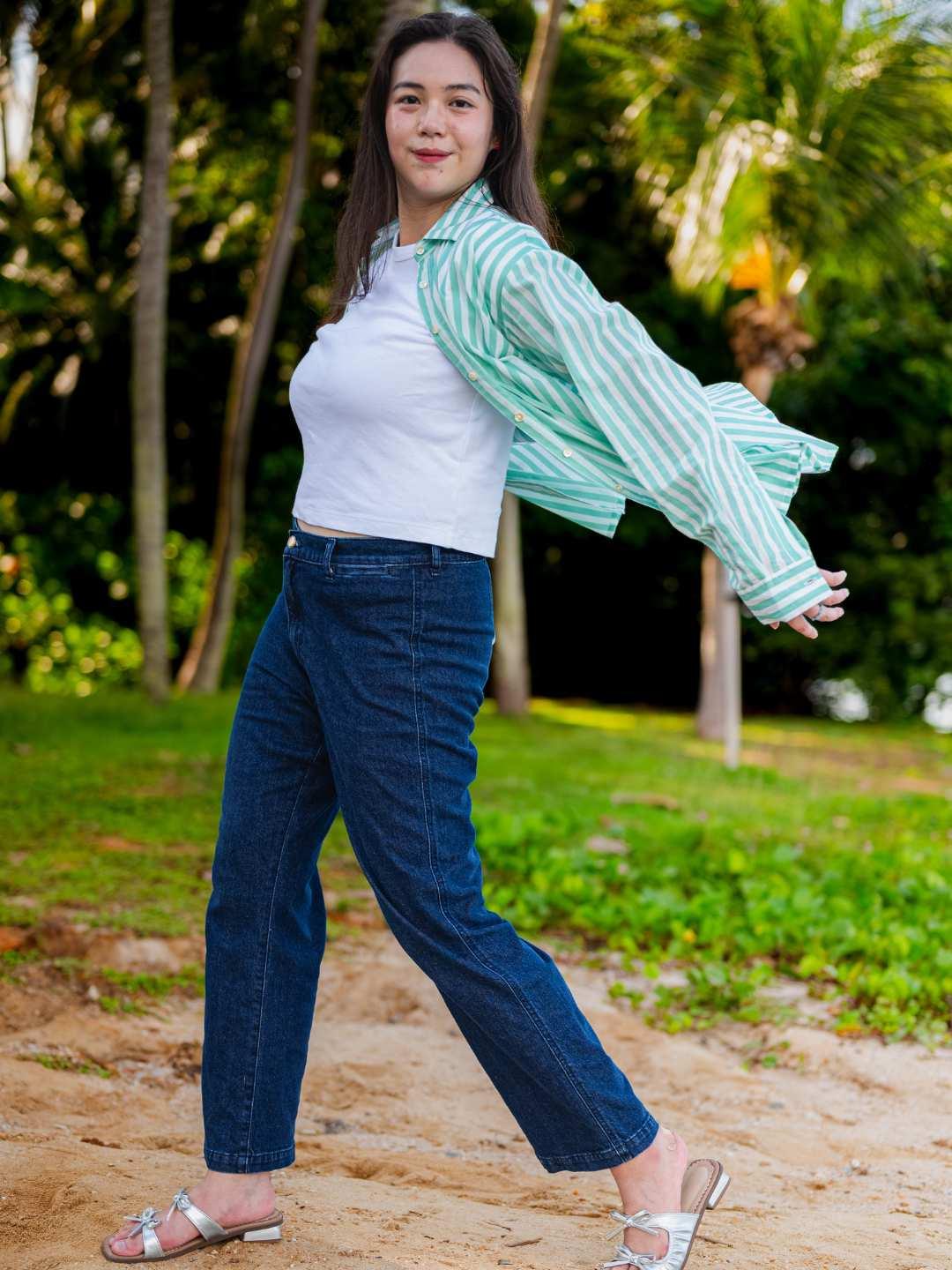 Woman wearing a white top and blue jeans with a striped green and white shirt in a park setting