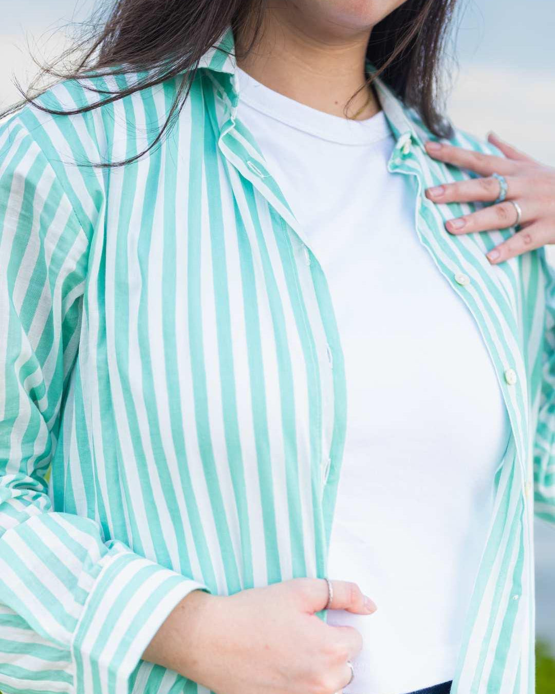 Person wearing a light blue and white striped shirt over a white top.