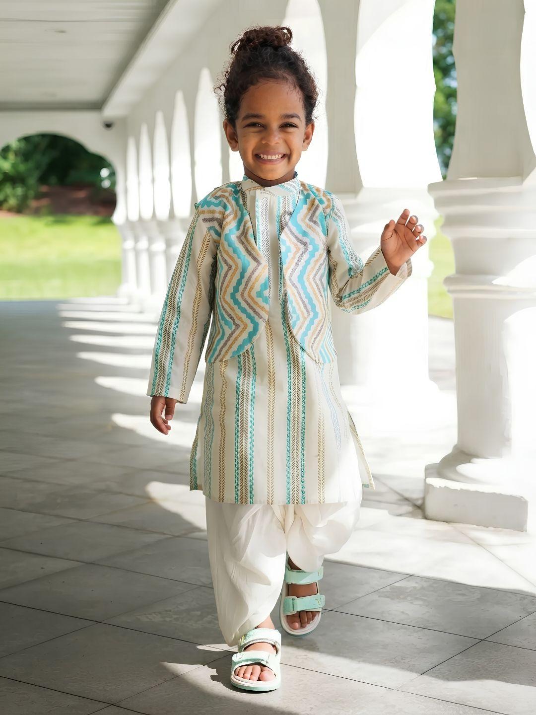 A young child walking on a covered walkway wearing a light beige traditional outfit with turquoise and white zigzag and vertical stripe patterns, paired with white pants and sandals.