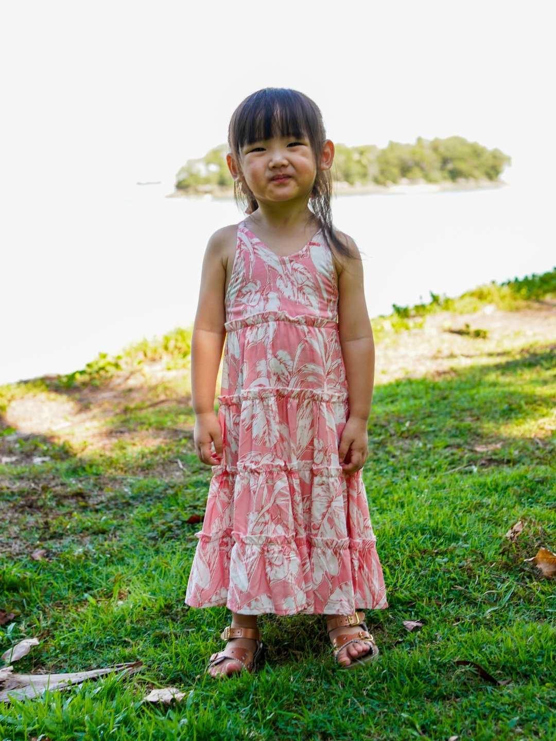 Girls' sustainable cotton long dress in rosy pink with tropical floral print, sleeveless and tiered design.