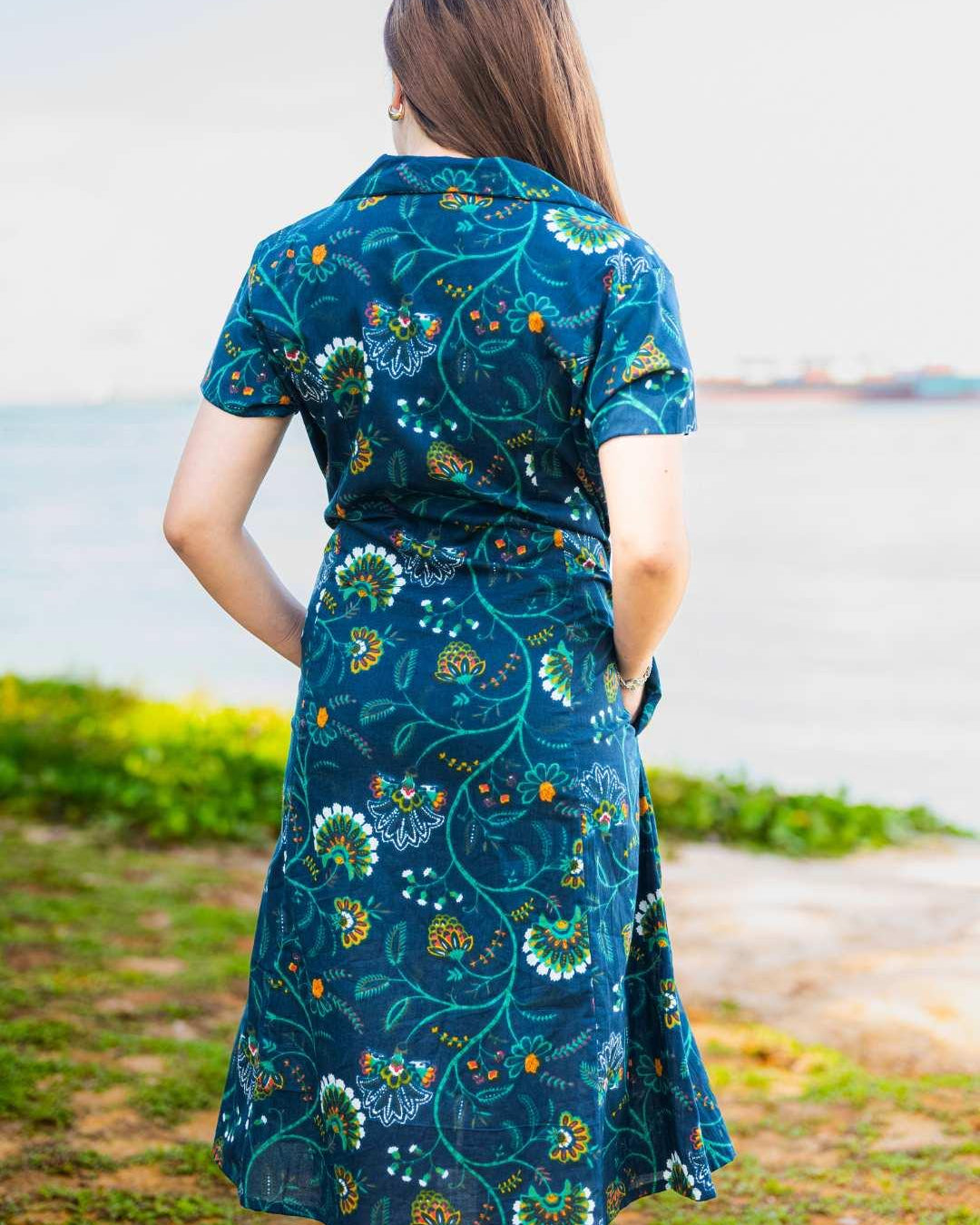 Woman wearing a blue floral dress standing by a body of water.