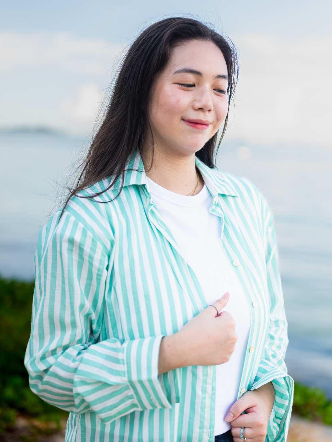 Woman wearing a green and white striped shirt by a body of water