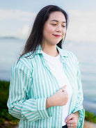 Woman wearing a green and white striped shirt by a body of water