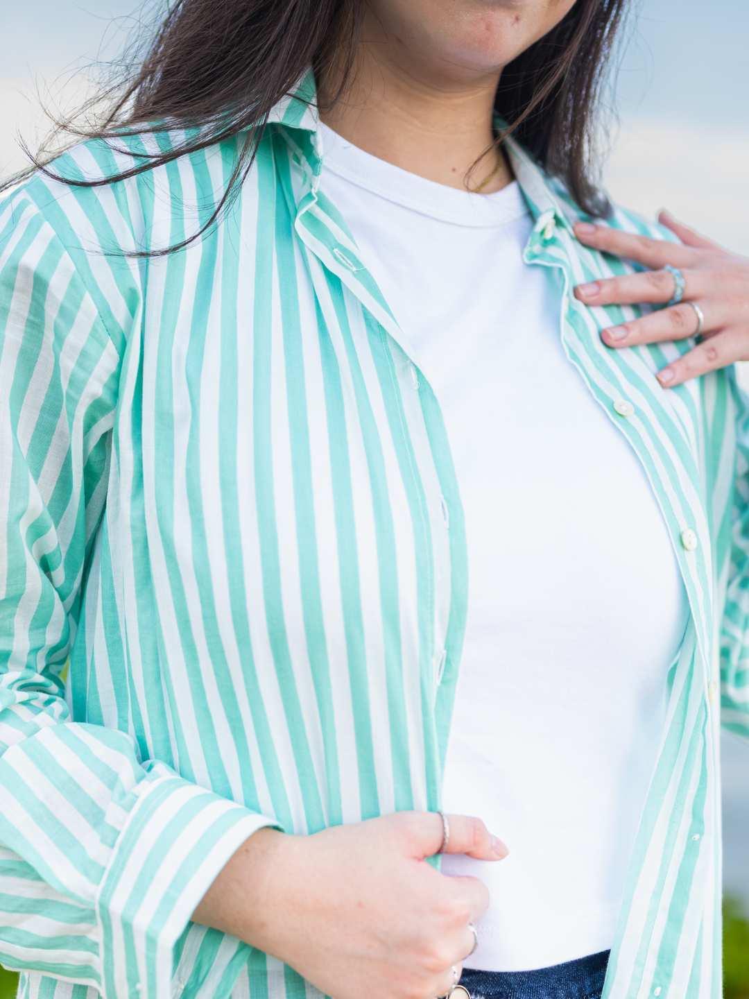 Person wearing a light blue and white striped shirt over a white top.