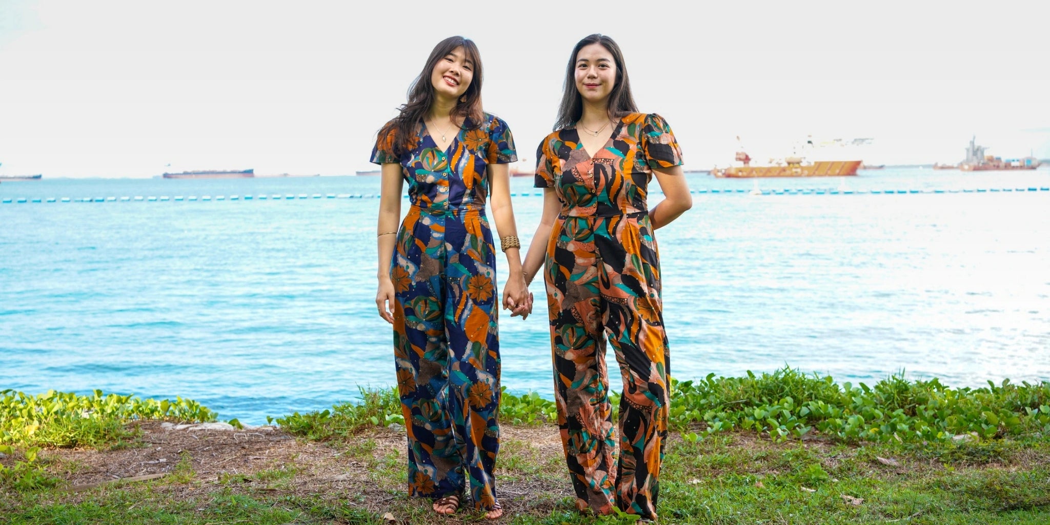 Two women in matching floral outfits standing by a body of water.