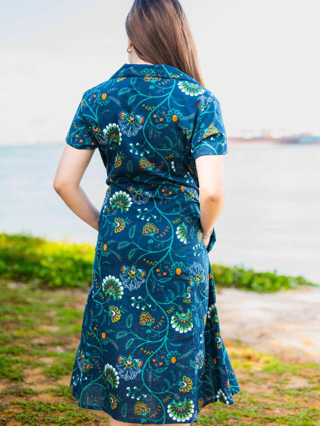 Woman wearing a blue floral dress standing by a body of water.